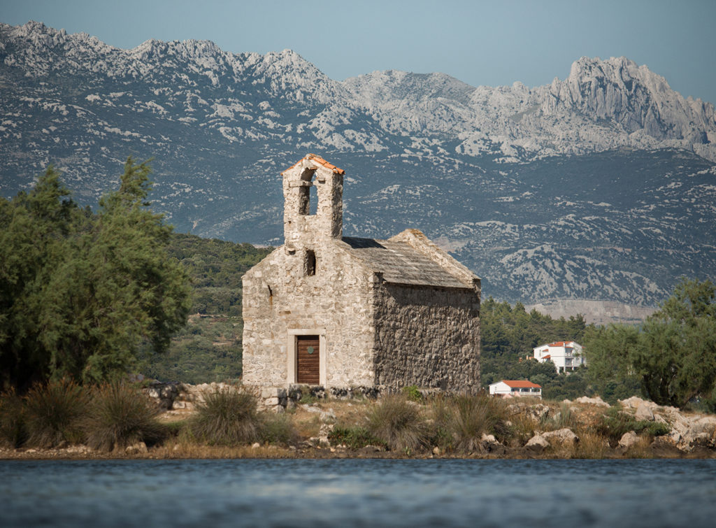 Kapelle Sv. Duh in Posedarje mit Velebit Gebirge im Hintergrund und unscharfem Meer im Vordergrund