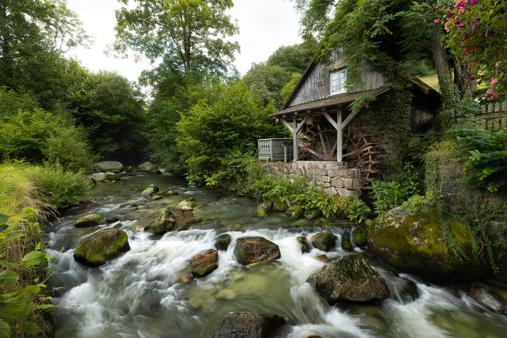 Rainbauernmühle im Schwarzwald mit grüner Umgebung und fließendem Bach im Vordergrund